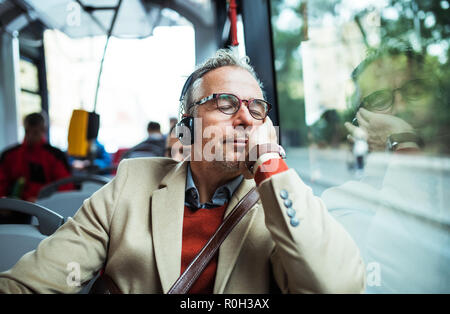 Mature tired businessman with heaphones travelling by bus in city.