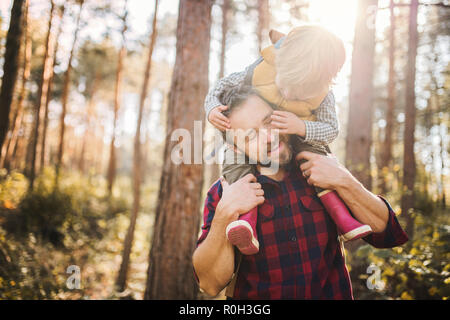 A mature father giving a toddler son a piggyback ride in an autumn forest.