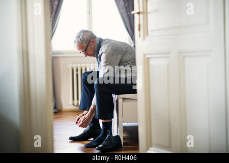 Mature businessman on a business trip sitting in a hotel room, tying shoelaces. Stock Photo