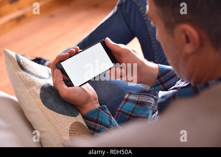 Adult man with blue shirt and jeans sitting on a sofa watching multimedia content on a smartphone. Raised viewpoint Stock Photo
