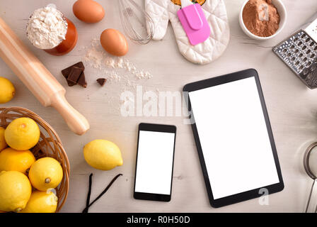 Pastry ingredients on a white wooden table and mobile devices. Concept of recipes in digital book. Horizontal composition. Top view Stock Photo