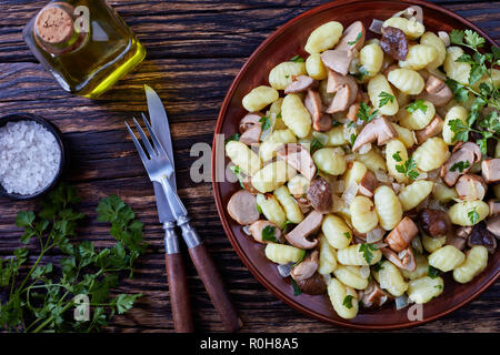 overhead view of  Potato gnocchi with porcini mushrooms served on a earthenware plate with fork and knife on a rustic wooden table, italian cuisine, h Stock Photo
