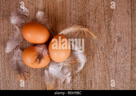 three eggs and feathers on rustic wooden table Stock Photo