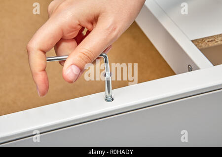 The furniture assembler tightens the cam bolt fixing into the furniture made of particle board with a hex wrench, flat pack furniture assembly. Stock Photo
