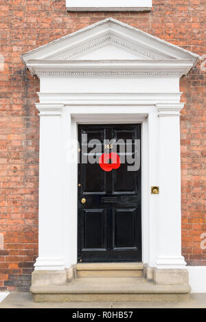 Large red remembrance poppy on smart black wooden door in large georgian-style door frame and surround in Ludlow, Shropshire Stock Photo