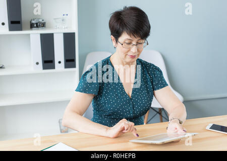 Business and people concept - middle aged confident woman is working with tablet in office Stock Photo