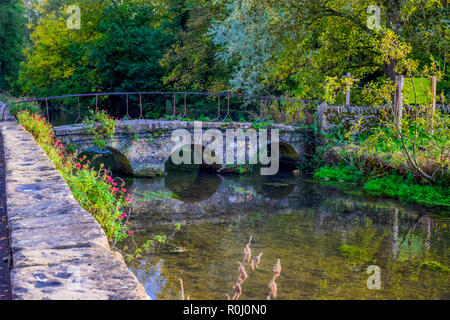 A small vintage stone bridge over river Coln that leads to Arlington Row of Bibury village in Cotswold district, Gloucestershire, England, UK Stock Photo