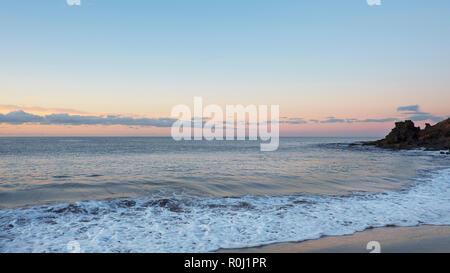 Tropical early morning sunrise on the beach with frothy waves, smooth sand and volcanic rocks, vacation destination concept Stock Photo