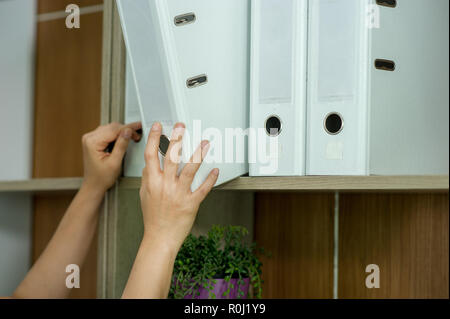 Hands and files of young employees Find something on the shelves. And his workspace. His white file Stock Photo
