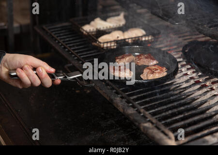 Close-up partial view of man holding frying pan with grilled steaks. cooking eats in a restaurant Stock Photo