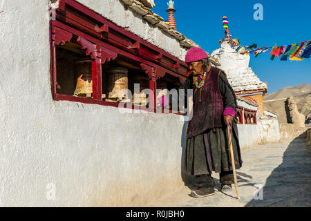 An old ladakhi woman is walking around Lamayuru Gompa, the oldest and largest existing monastery in Ladakh, turning prayer wheels for religeous reason Stock Photo