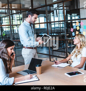 young businessman using digital tablet and looking at smiling female colleague at workplace Stock Photo