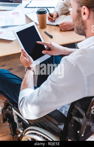 partial view of businessman in wheelchair using tablet with blank screen at workplace in office Stock Photo