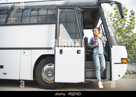 beautiful asian woman with backpack walking out from travel bus at urban street Stock Photo