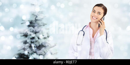 christmas smiling doctor with smart phone on blurred lights with tree Stock Photo