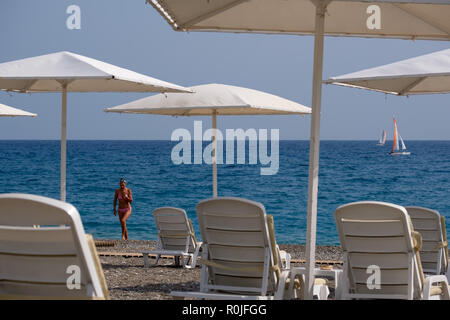 Tan woman leaving the water on the pebble beach at Club Med Palmiye luxury all inclusive resort, Kemer, Antalya, Turkey Stock Photo