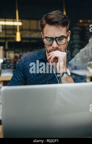 Entrepreneur sitting in restaurant working seriously on his laptop. businessman looking tensed working on his laptop wearing earphones. Stock Photo