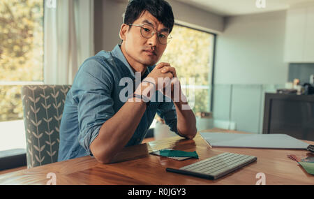 Portrait of creative man sitting at is desk with computer keyboard and fabric samples. Confident architect at his desk looking at camera. Stock Photo