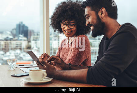 businessman and woman sitting in office discussing work using a tablet computer. Happy business coworkers sitting at work desk doing work. Stock Photo