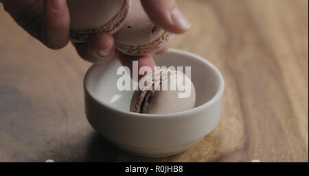 man hand put beige macarons in white bowl on wood table, wide photo Stock Photo