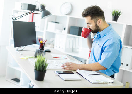 The young man is in the office at the computer table, drinking coffee and working with a magnetic Board. Stock Photo