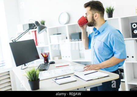The young man is in the office at the computer table, drinking coffee and working with a magnetic Board. Stock Photo