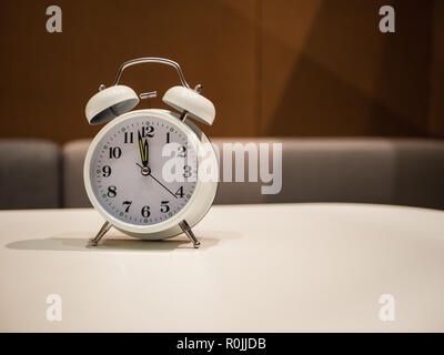 Vintage Alarm Clock standing on a white desk with brown blurry sofa in background Stock Photo