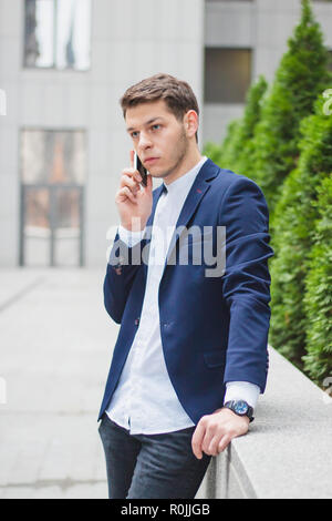 Business style. A young businessman is talking on the phone from the street. The guy in the blue jacket Stock Photo