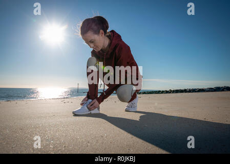 woman jogger tying up her trainers before running on the beach Stock Photo