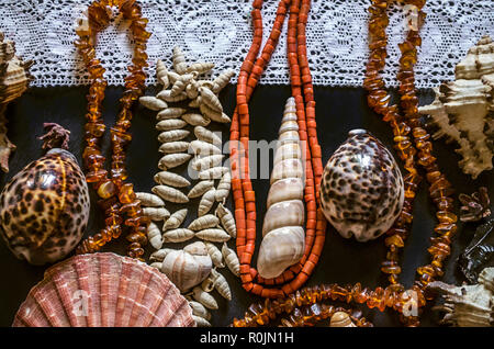 Various shells and stones with beads of red coral and small amber on the white openwork border lie on black plywood Stock Photo