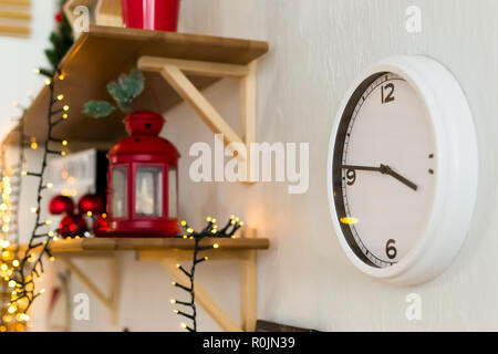 white wall clock. on a wooden shelf red metal candlestick. the new year is 2019. garland and red Christmas balls in a white plate. Stock Photo