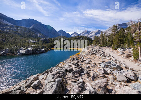 Hiking trail following the shoreline of an alpine lake surrounded by the rocky ridges of the Eastern Sierra mountains; Box Lake, Little Lakes Valley t Stock Photo