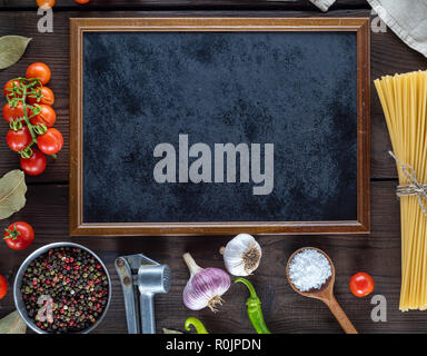 empty black frame and ingredients for cooking pasta on a brown wooden table, copy space Stock Photo