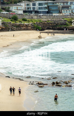 Bondi to Coogee coastal walk and people walking on the sand of Bronte Beach and dwellings on sandstone cliff over Pacific Ocean Sydney NSW Australia.