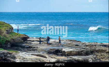 Bondi to Coogee coastal walk people standing on sandstone rocks over Pacific Ocean Sydney NSW Australia.