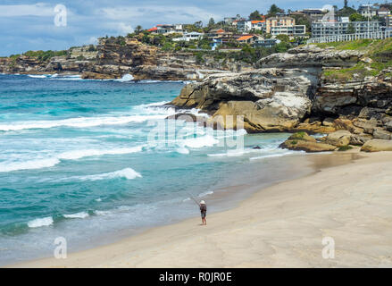 Lone male fisherman fishing with a fishing rod from the sandy Bronte Beach Sydney NSW Australia. Stock Photo