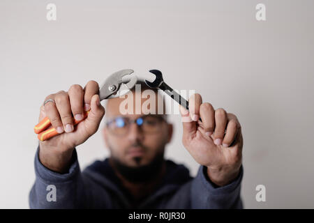 Out of focus man holding wrench and pliers in hand Stock Photo