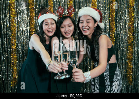 ladies with glasses of champagne cheers at xmas party. cheerful young girls celebrating christmas eve at nightclub. Smiling friends having drinks duri Stock Photo
