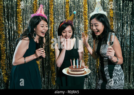 Happy friends celebrating birthday with cake beer and champagne in night club. young ladies wearing hats blowing candles together on the stage. girls  Stock Photo