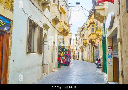 VICTORIA, MALTA - JUNE 15, 2018: The curved narrow shopping street with small stores, offering local souvenirs, accessories, foods and handicraft piec Stock Photo