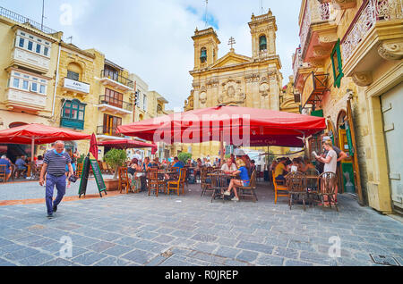 VICTORIA, MALTA - JUNE 15, 2018: The St George square with cozy outdoor cafes, souvenir stores and impressive facade of St George basilica with carved Stock Photo