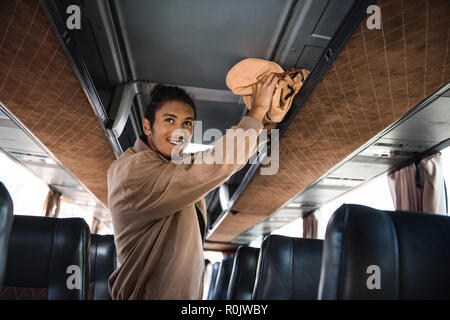 smiling young multiracial man putting rucksack on shelf in travel bus Stock Photo