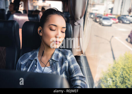 young asian woman sleeping and listening music in earphones during trip on travel bus
