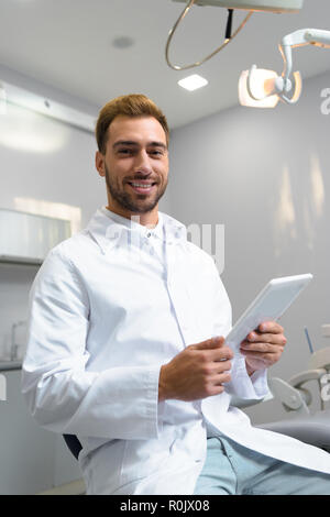 happy young dentist in coat using tablet in office Stock Photo