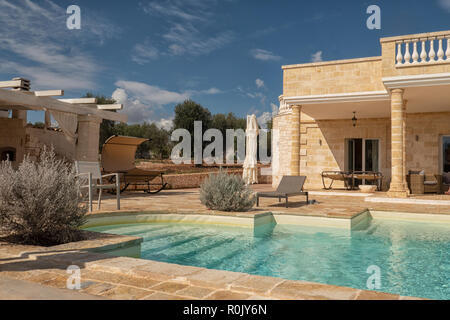 Mock greek classic villa wih balcony against a blue sky and a swimming pool with feet in front of them Stock Photo