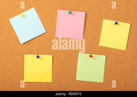 colorful papers pined with tacks on brown cork board background. Stock Photo