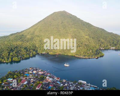 A Pinisi schooner sits at anchor next to Banda Api, a live volcano in the Banda Sea, Indonesia. Stock Photo