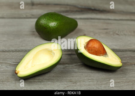 Two avocados, one cut in half, seed visible, on gray wood desk table Stock Photo