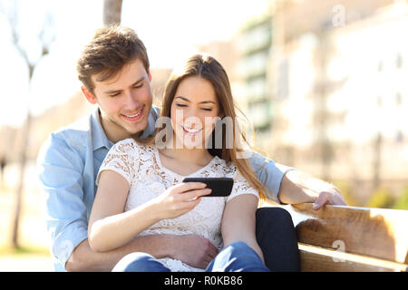 Happy couple listening to music together sitting on a bench in a park