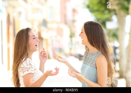 Side view portrait of two happy friends talking and lauging in the street Stock Photo